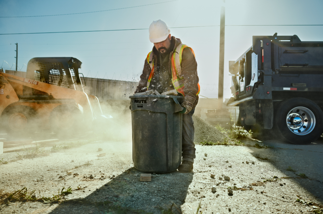 Construction worker handling trash bin outdoors.